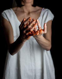Midsection of woman with blood hands against black background