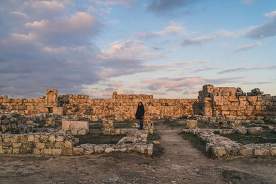 Full length of woman standing by old ruins against cloudy sky