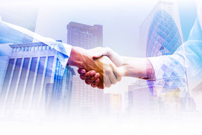 Digital composite image of business colleagues shaking hands against modern buildings