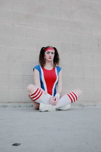 Portrait of cheerleader sitting on footpath against wall