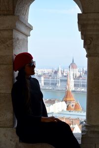 Side view of woman sitting on window sill