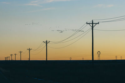 Silhouette electricity pylons against sky during sunset