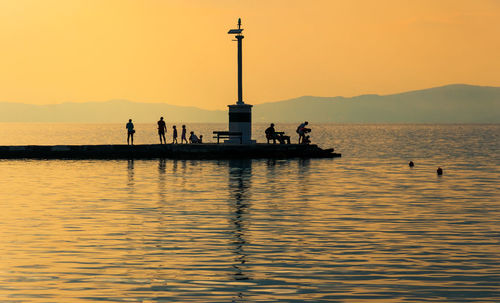 Silhouette people on boat in sea against orange sky