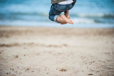 Low section of boy jumping on sand at beach