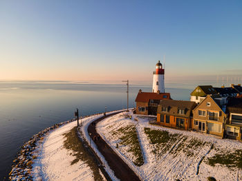 Lighthouse by sea against clear sky during sunset