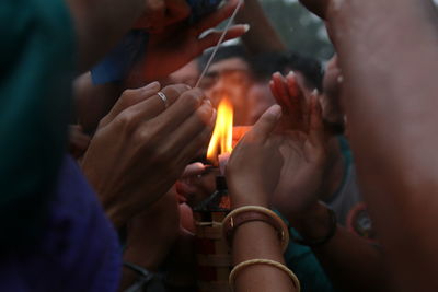 Close-up of hands by lit diya