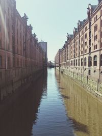 Canal in city against clear sky