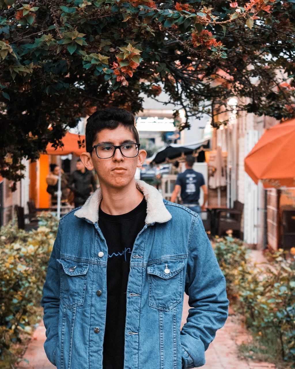 front view, looking at camera, one person, young adult, portrait, casual clothing, young men, tree, real people, standing, plant, glasses, waist up, eyeglasses, day, architecture, lifestyles, focus on foreground, nature, outdoors