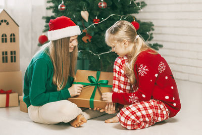 Two happy and cheerful sisters in fashionable new year's outfits open gifts at home 