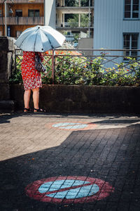 Rear view of woman with umbrella standing on footpath