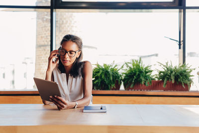 Businesswoman using digital tablet while talking on phone at office