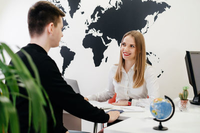 Travel agent having a client in light modern office of tour agency, giving passport after 