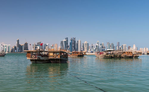 Boats in sea by city against clear sky