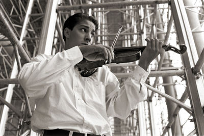 Low angle view of man playing violin while standing by built structure