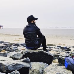 Man sitting on rock at beach against clear sky