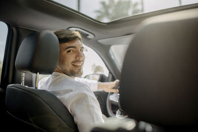 Happy man looking over shoulder sitting in electric car