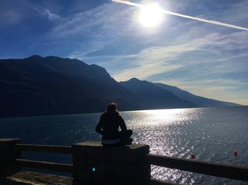 Rear view of woman sitting on railing against sky