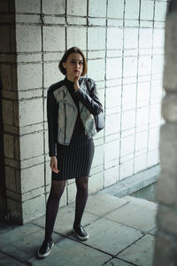 Portrait of young woman wearing jacket while standing against patterned wall