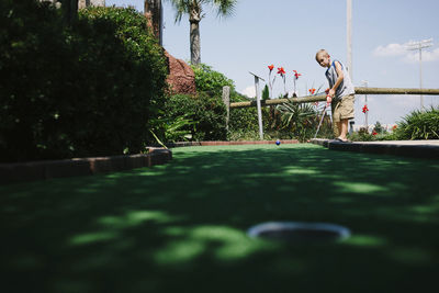 Boy playing miniature golf against sky