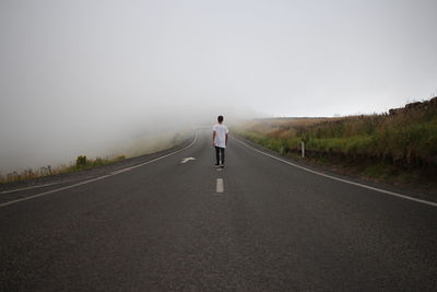 Rear view of man walking on road against sky