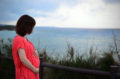 View of pregnant woman standing by sea against sky