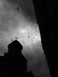 Low angle view of birds flying against cloudy sky