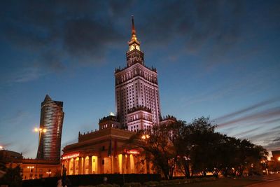 Illuminated palace of culture and science and modern building against sky at dusk