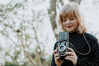 Low angle view of woman holding camera in forest