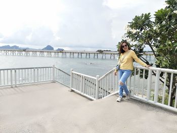 Full length of woman standing on railing against sky