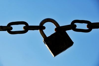 Low angle view of padlock attached to chainlink against sky