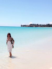 Rear view of woman standing by sea against clear sky