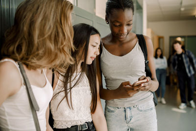 Junior high students using smart phone while standing in school corridor