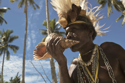 Low angle view of man blowing conch shell against sky