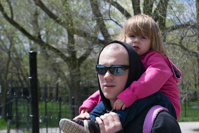 Man carrying daughter on shoulder against trees during sunny day