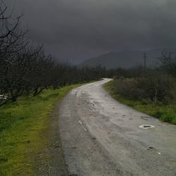 Road passing through field against cloudy sky