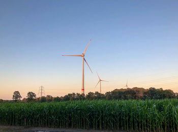 Wind turbines on field against clear sky during sunset