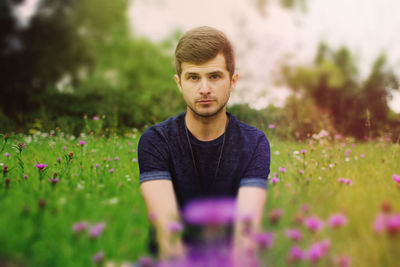 Portrait of young man amidst purple flowers blooming on field