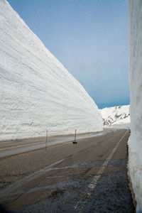 Road by snow covered land against clear sky