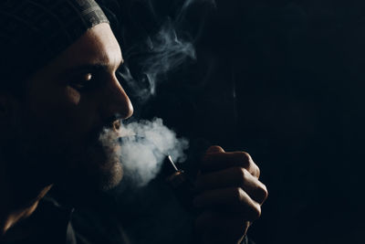 Portrait of man smoking cigarette against black background