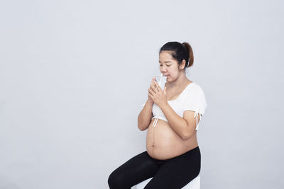 Young woman looking away while standing against white background