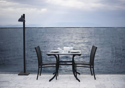 Chairs and table by sea against sky