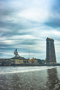 View of buildings by river against cloudy sky