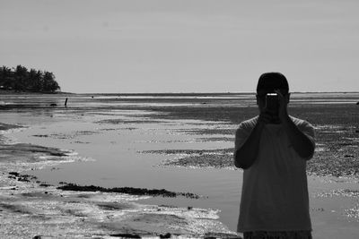 Rear view of man standing on beach against clear sky
