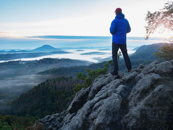 Hiker man climbed up alone to exposed summit above heavy fog. biig adventure in wild nature