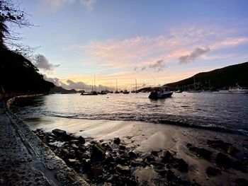 Sailboat on sea shore against sky during sunset