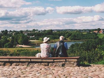 Rear view of senior couple sitting on bench against sky at park