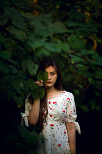 Portrait of young woman hiding eye with leaf in forest