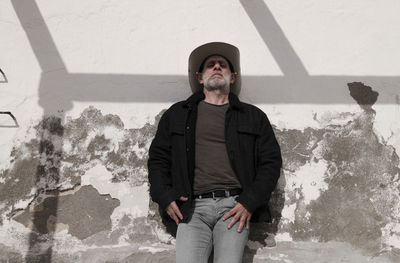 Portrait of adult man in cowboy hat and jeans against wall with sunlight and shadow. almeria, spain