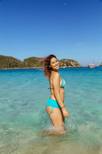 Smiling woman wading in sea against clear sky