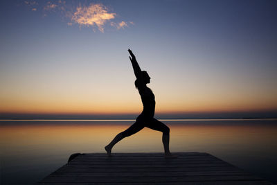 Silhouette woman exercising on pier against sky during sunset